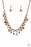 Featuring pearly and glassy finishes, an array of brass, brown, and orange beads swing from a double-linked brass chain, creating a fancy fringe below the collar. Features an adjustable clasp closu