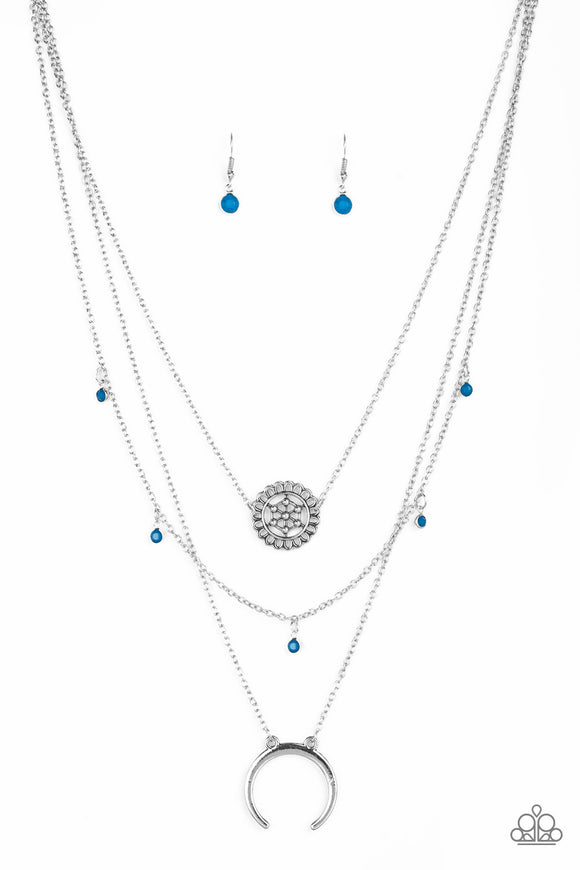 A silver floral frame swings from the uppermost chain, above a strand of faceted blue beads swinging from a shimmery silver chain. A silver crescent frame swings from the lowermost chain, creating whimsical layers down the chest. Features an adjustable clasp closure.