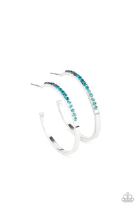 The front half of a dainty silver hoop is encrusted in an ombre of blue rhinestones, creating a sparkly spectrum of color. Earring attaches to a standard post fitting. Hoop measures approximately 1 1/2" in diameter.