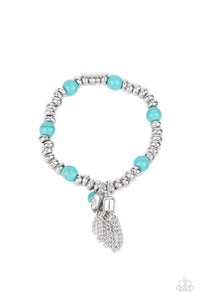 An earthy collection of hammered silver beads and round turquoise stones are threaded along a stretchy band around the wrist. A dainty silver tassel, hammered silver disc, and a turquoise stone swing from the seasonal display, adding playful movement to the whimsy look.