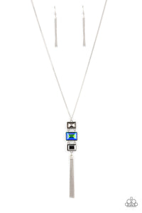 A sparkly collection of mismatched smoky, blue, and hematite rectangular gems stack at the bottom of a lengthened silver chain, creating a glamorous pendant. A dainty silver chain tassel swings from the bottom, adding glamorous movement to the modern display. Features an adjustable clasp closure