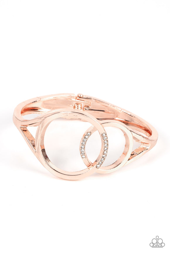 Encrusted in sections of glassy white rhinestones, two oversized rose gold rings delicately overlap across the center of the wrist, resulting in a timeless bangle-like bracelet around the wrist. Features a hinged closure.