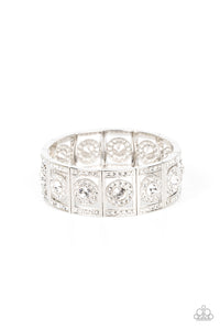 A glassy white rhinestone is pressed into a ring of glitzy white rhinestones inside a rectangular silver frame dusted in dazzling white rhinestones. The timeless frames sparkle along stretchy bands around the wrist, resulting in a glamorously glittering centerpiece.