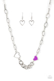 A pair of shiny silver and purple hearts asymmetrically adorn sections of mismatched silver chain, resulting in a flirtatious pop of color below the collar. Features an adjustable clasp closure.