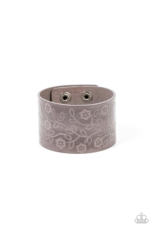 A flowery and leafy motif blooms across the front of a distressed gray leather band, resulting in a rustic floral centerpiece around the wrist. Features an adjustable snap closure.