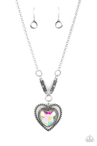 Bordered in spun silver ribbons, an oversized iridescent heart gem is pressed into a silver heart frame below the collar. The flirtatious pendant attaches to silver rings and decorative silver frames dotted in matching iridescent rhinestones, resulting in a dash of vintage inspired romance. Due to its prismatic palette, color may vary. Features an adjustable clasp closure.