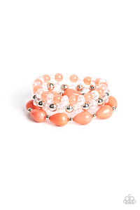 A whimsical assortment of crystal-like beads, silver beads, opaque coral beads, and coral teardrop beads are threaded along stretchy bands around the wrist, resulting in colorful layers.