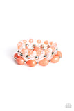 A whimsical assortment of crystal-like beads, silver beads, opaque coral beads, and coral teardrop beads are threaded along stretchy bands around the wrist, resulting in colorful layers.