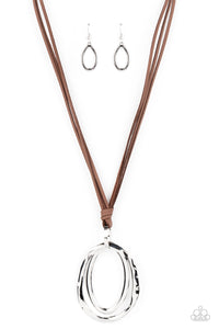 Long strips of brown leather knot around a silver link where a mismatched pair of smooth and hammered silver ovals swing from the bottom, resulting in a rustic pendant. Features an adjustable clasp